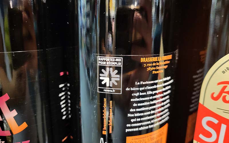 Photo du Piucto du réemploi sur l'étiquette une bouteille en verre, dans un point de vente et de collecte